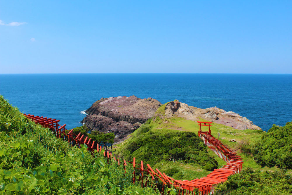 元乃隅稲成神社の赤い鳥居と青い空と海、緑の丘のコントラストが美しい